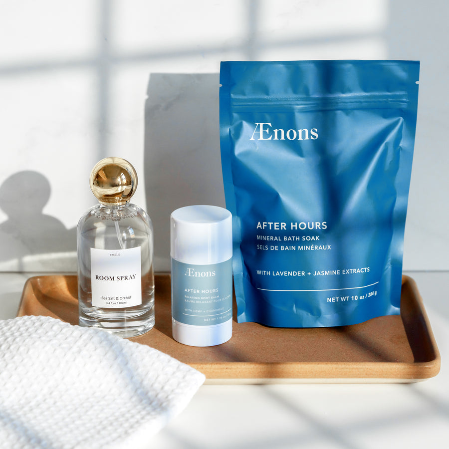 A bottle of room spray, relaxing body balm, and mineral bath salts on a wooden vanity tray.
